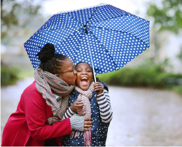 Young girl holding an umbrella while being kissed on the cheek by a lady